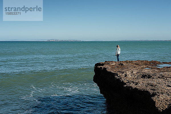 Mädchen steht auf einer Klippe mit Blick auf den Ozean