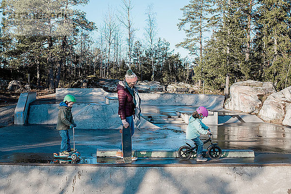 Mama und ihre Kinder fahren in einem Skatepark und haben Spaß in der Sonne