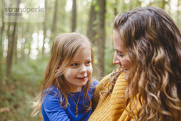 Ein kleines Mädchen schmiegt sich in die Arme seiner Mutter  während sie zusammen lächeln