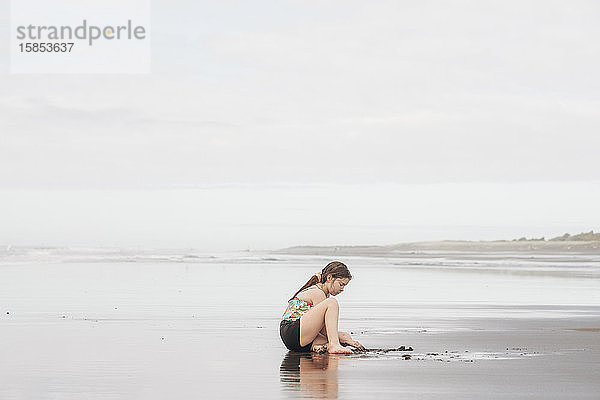 Junges Mädchen sitzt und spielt im Sand am Strand