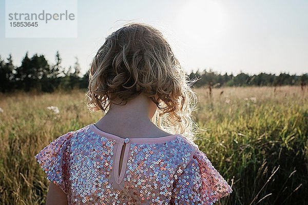 Der Rücken eines jungen Mädchens  das in einem funkelnden Kleid durch ein Feld läuft