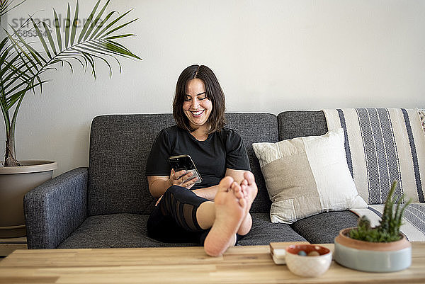 Frau sitzt mit erhobenen Füßen auf der Couch am Telefon