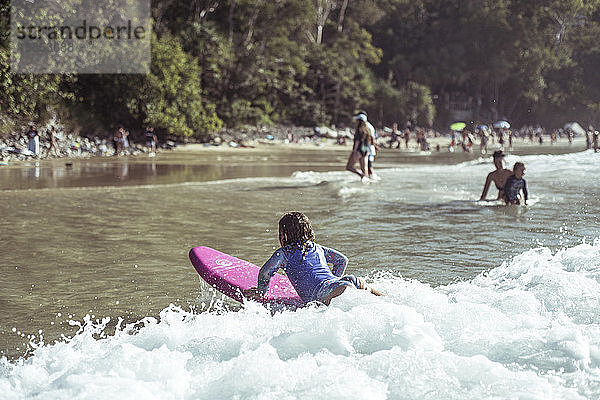 Junges Mädchen fängt Welle auf dem Kinder-Surfbrett schöne Strandbucht