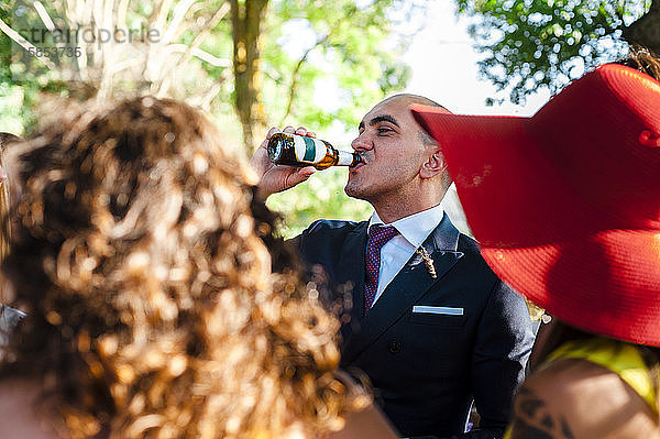 Durstiger Bräutigam trinkt nach der Hochzeit von Gästen umgeben Bier