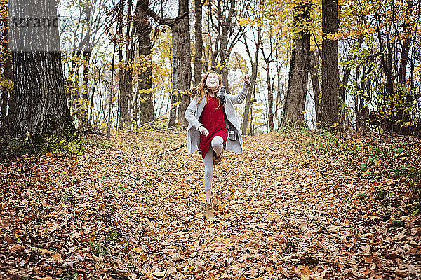 Junges rothaariges Mädchen spielt draußen im Herbstlaub