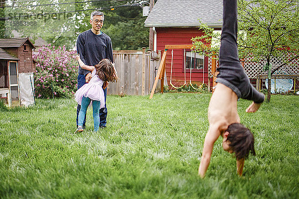 Ein Vater spielt mit kleinem Mädchen im Hof  während der Junge Purzelbäume schlägt