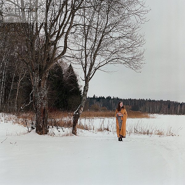 Eine Frau steht am Ufer eines zugefrorenen Sees in einem gelben Schal