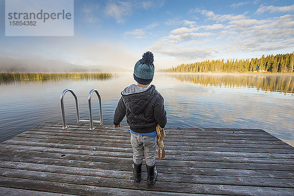 Junge steht am Dock und schaut auf einen ruhigen See