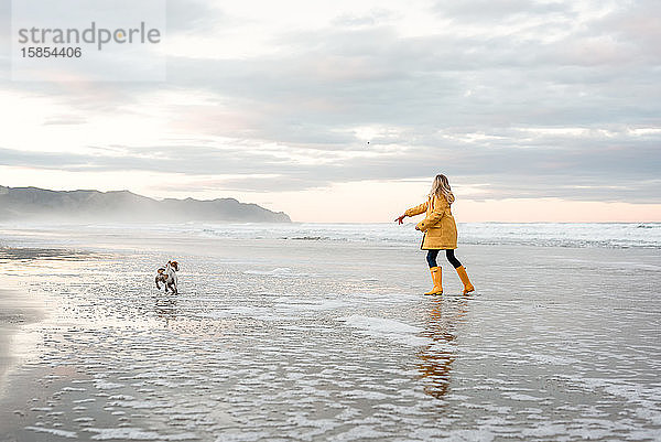 Mädchen im Vorschulalter spielt mit Hund am Strand in Neuseeland