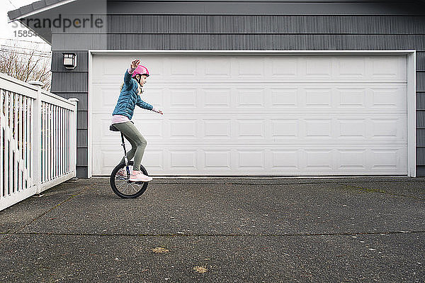 Mädchen balanciert auf einem Einrad auf der Auffahrt vor der Garage