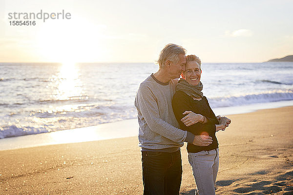 Zärtliches älteres Ehepaar  das bei Sonnenuntergang am Strand steht