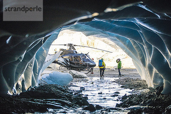 Ehepaar nähert sich nach der Erkundung einer Eishöhle einem Hubschrauber.