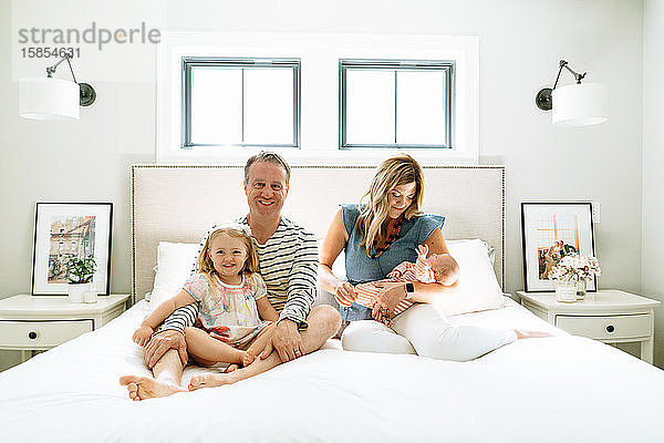 Geradeaus Porträt einer vierköpfigen Familie  die zusammen auf einem Bett sitzt