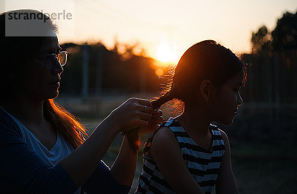 Die Mutter frisiert das Haar ihrer Tochter während des Sonnenuntergangs