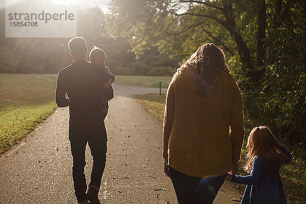 Eine Familie geht in einem Park in der untergehenden Sonne an den Händen haltend zusammen