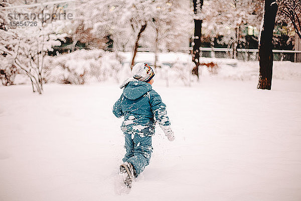 Rückansicht eines Jungen  der im Winter auf einem schneebedeckten Feld im Park läuft
