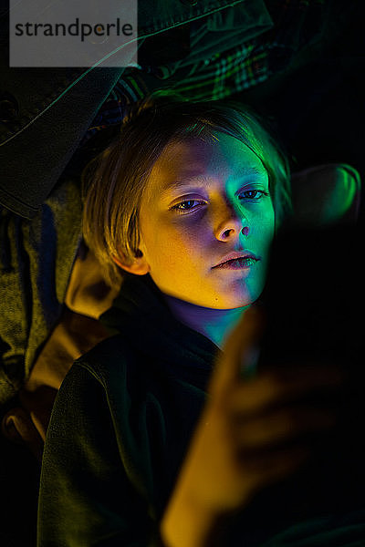 Bildnis eines Tween beim Betrachten einer Tablette mit farbigem Lichtstich im Gesicht