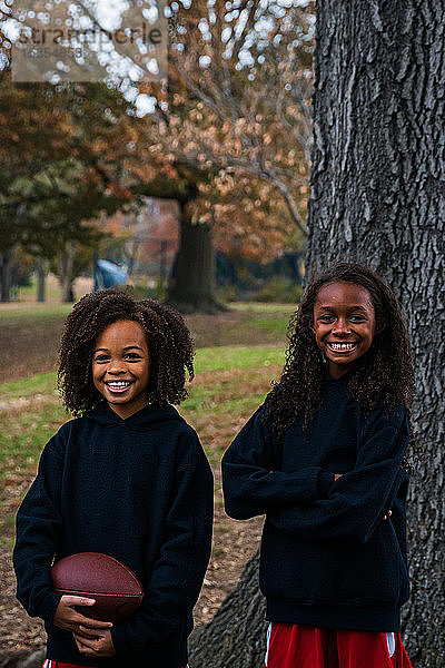 Porträt von lächelnden Schwestern mit American Football im Park