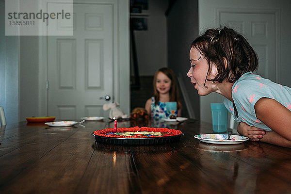 Seitenansicht eines Mädchens  das eine Kerze auf einem Geburtstagskuchen ausbläst