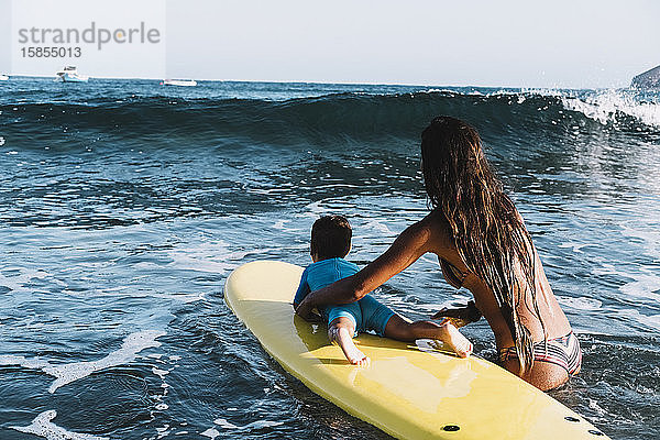 Rückenansicht von Mutter und Sohn auf einem Surfbrett auf See