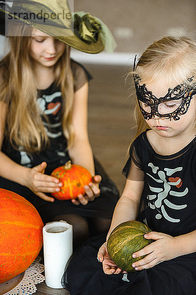 Zwei Schwestern zu Halloween in Skelettkostümen mit Kürbissen gekleidet