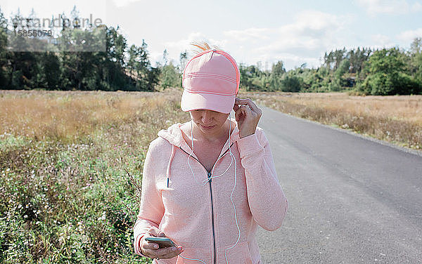 Frau  die mit ihrem Telefon und Kopfhörern eine Landstraße entlang läuft
