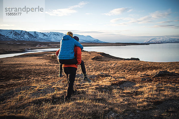 Mann trägt Frau huckepack im Feld mit Bergen im Hintergrund