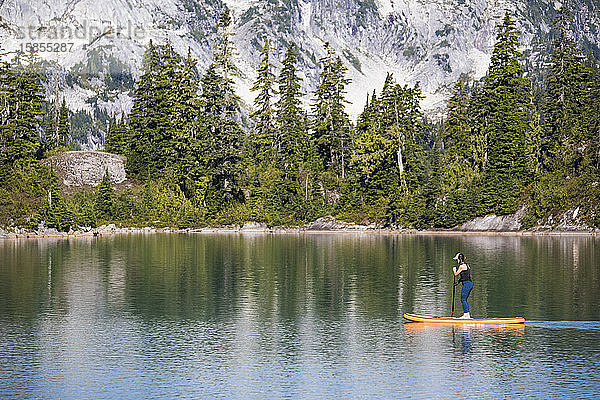 Seitenansicht einer aktiven Frau beim Paddelbootfahren auf einem Bergsee.