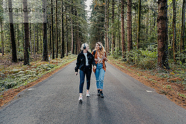 Zwei Frauen gehen auf einer Straße im Wald spazieren  während sie Musik hören