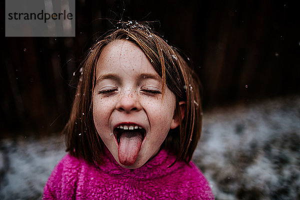 junges Mädchen  das im Winter versucht  Schneeflocken auf der Zunge zu fangen