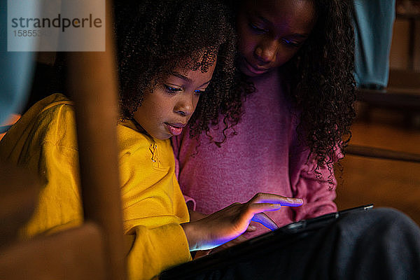 Mädchen spielt zu Hause Videospiel mit Schwester auf digitalem Tablet