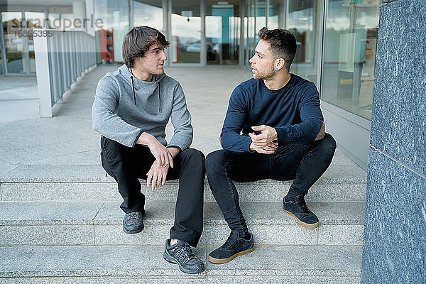 Frontansicht von zwei jungen Männern  die sich auf einer Stadttreppe sitzend unterhalten