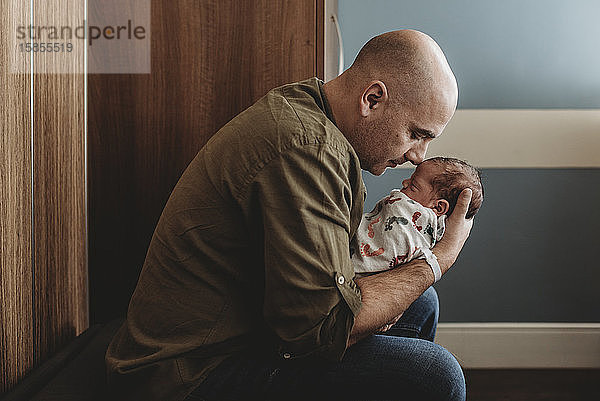 Seitenansicht eines glücklichen Vaters  der seinen neugeborenen Sohn im Krankenhaus umarmt