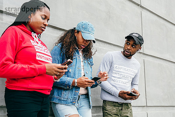 Städtische Freunde schauen sich Smartphones draußen an der Wand an
