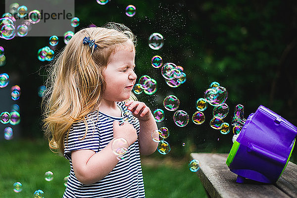 Ein kleines Mädchen steht vor einer Seifenblasenmaschine.