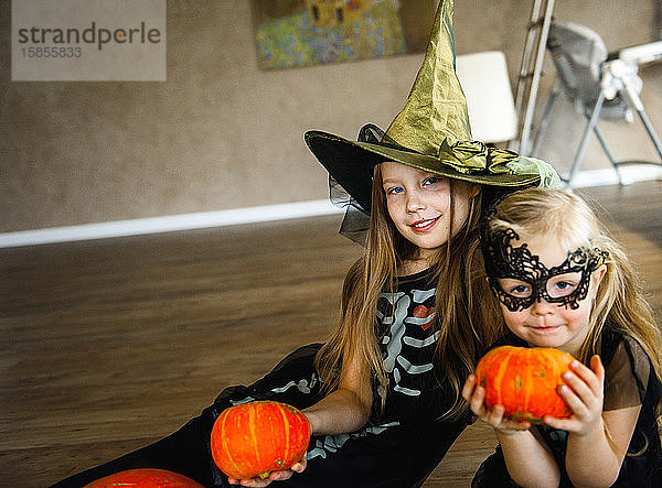 Zwei Schwestern zu Halloween in Skelettkostümen mit Kürbissen gekleidet