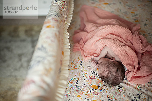Draufsicht auf ein neugeborenes Mädchen  das in einer rosa Decke in einem Kinderbett schläft