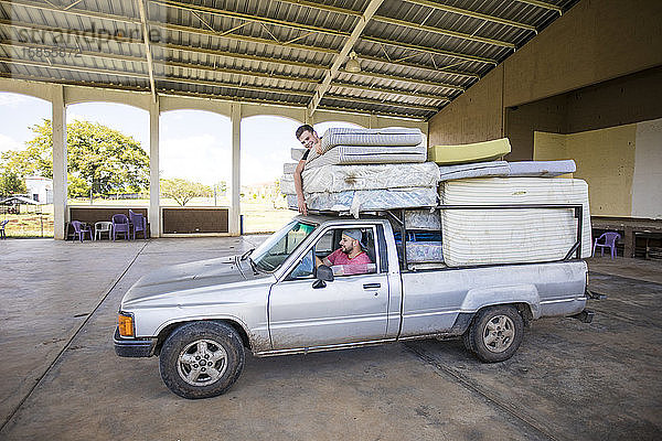 Zwei Männer  die auf einem beladenen Lastwagen mitfahren  helfen beim Transport von Matratzen im Waisenhaus.