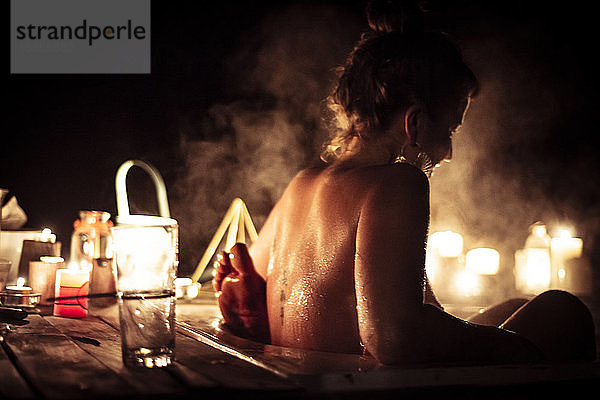 Junge Frau im dampfenden Freibad mit Partner bei Kerzenlicht