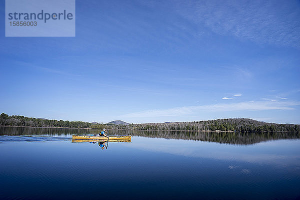 Mann paddelt mit einem Kanu unter klarem blauen Himmel auf einem ruhigen See