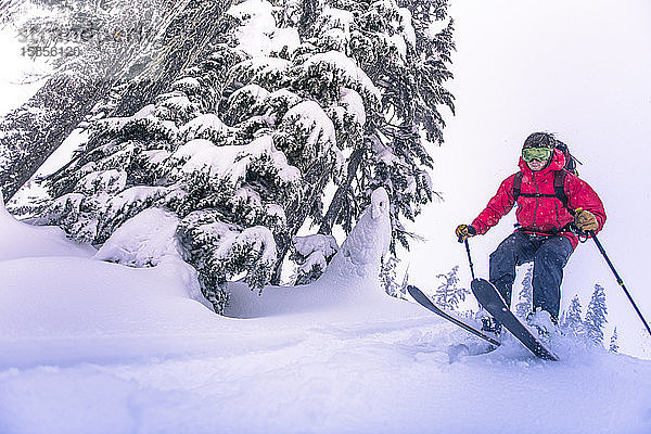 Mann springt vom Gipfel eines verschneiten Hügels beim Skitourengehen in BC
