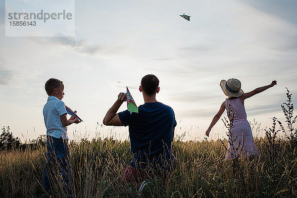 Vater spielt mit seinem Sohn und seiner Tochter bei Sonnenuntergang Papierflieger