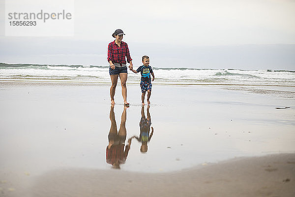 eine Mutter  die am Strand spazieren geht und mit ihrem Sohn Händchen hält.