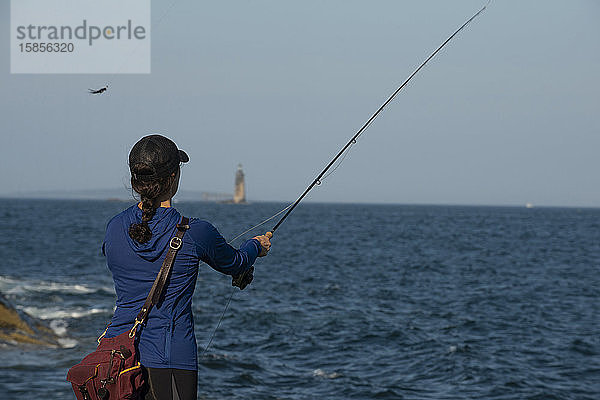 Frau im blauen Hemd beim Fliegenfischen an der Küste von Maine.