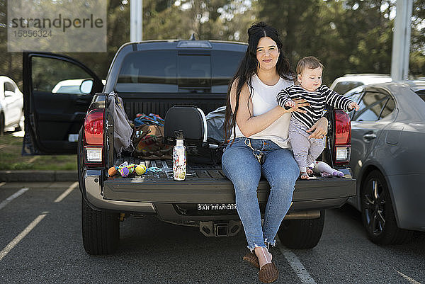 Eine junge Frau und ihr Baby sitzen auf der Heckklappe eines Lastwagens an einer Raststätte.