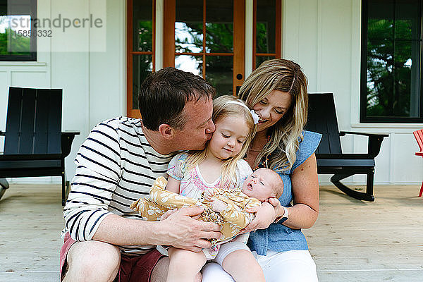 Ein Mädchen im Kleinkindalter hält ihre kleine Schwester mit Mama und Papa