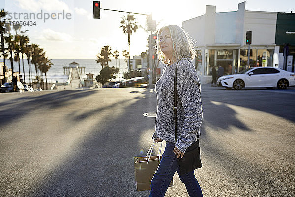 Seitenansicht einer älteren Frau mit Einkaufstasche  die bei Sonnenuntergang in der Stadt auf der Straße geht