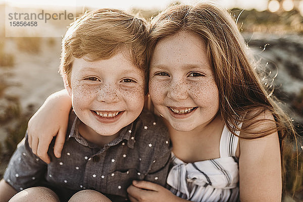 Porträt von jungen rothaarigen sommersprossigen Geschwistern  die bei Sonnenuntergang lächeln