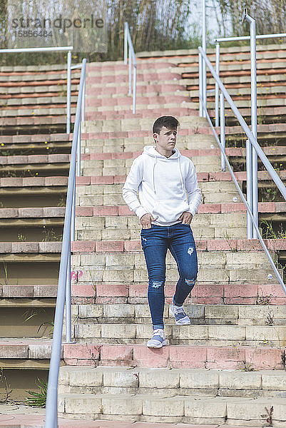 Junger männlicher Teenager  der mit den Händen auf der Tasche die Treppe hinuntergeht und dabei wegschaut