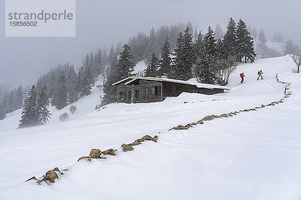 In einer Winterlandschaft kommen zwei Wanderer in der Nähe einer Berghütte